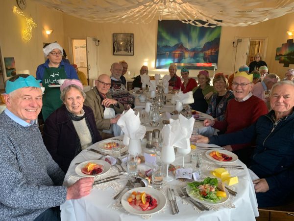 Group of people sitting down for a Christmas Lunch at Wydale Hall. Smiling faces, Christmas cracker hats, starters on the table.